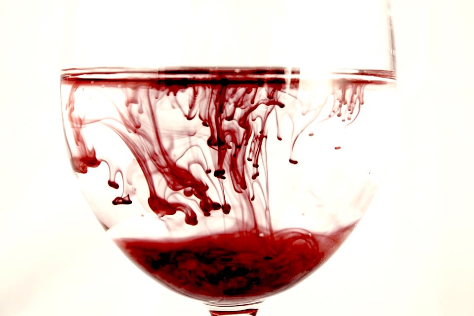 Red fluid spreading within wine glass